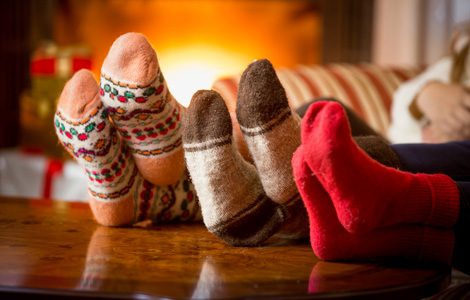 Three pairs of sock-covered feet sit on a coffee table with a fire in the background.