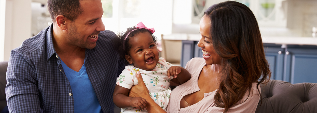 A young african american couple holding their baby girl as they sit on a couch.