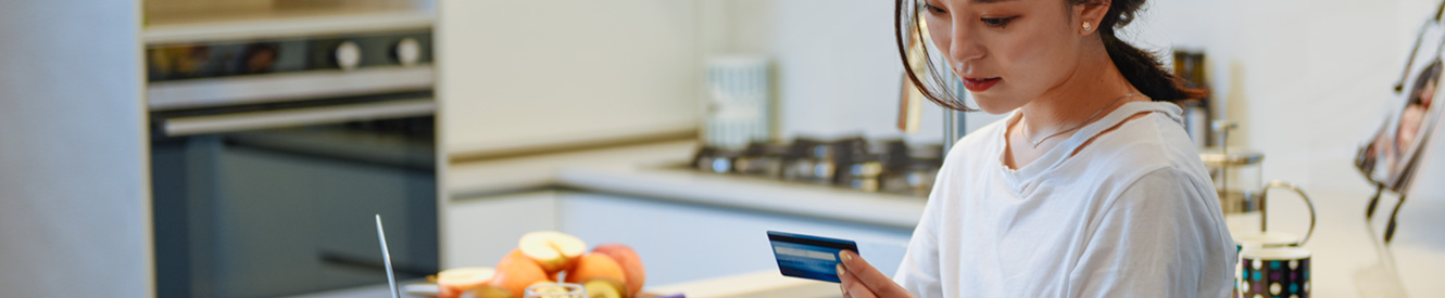 A woman looks at her credit card while also using a laptop.