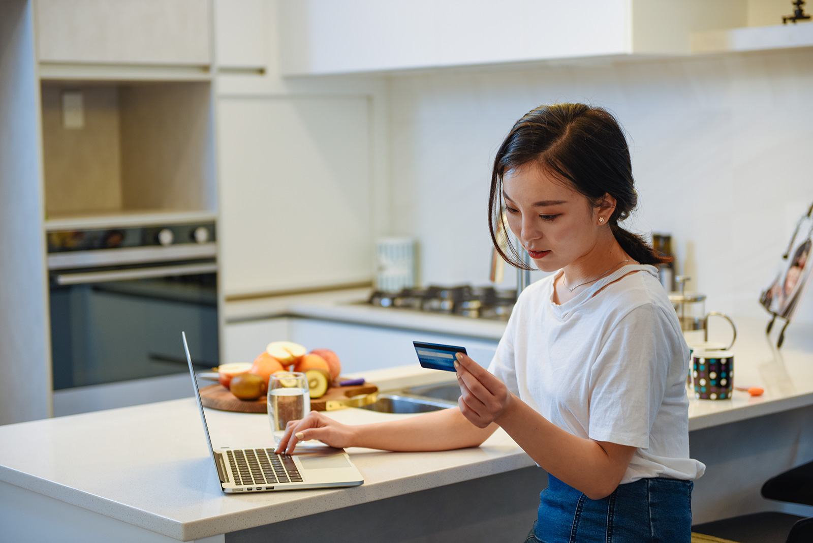 A woman looks at her credit card while also using a laptop.